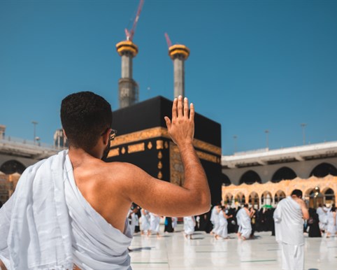 Pilgrim in ihram reaching toward the Kaaba in Makkah